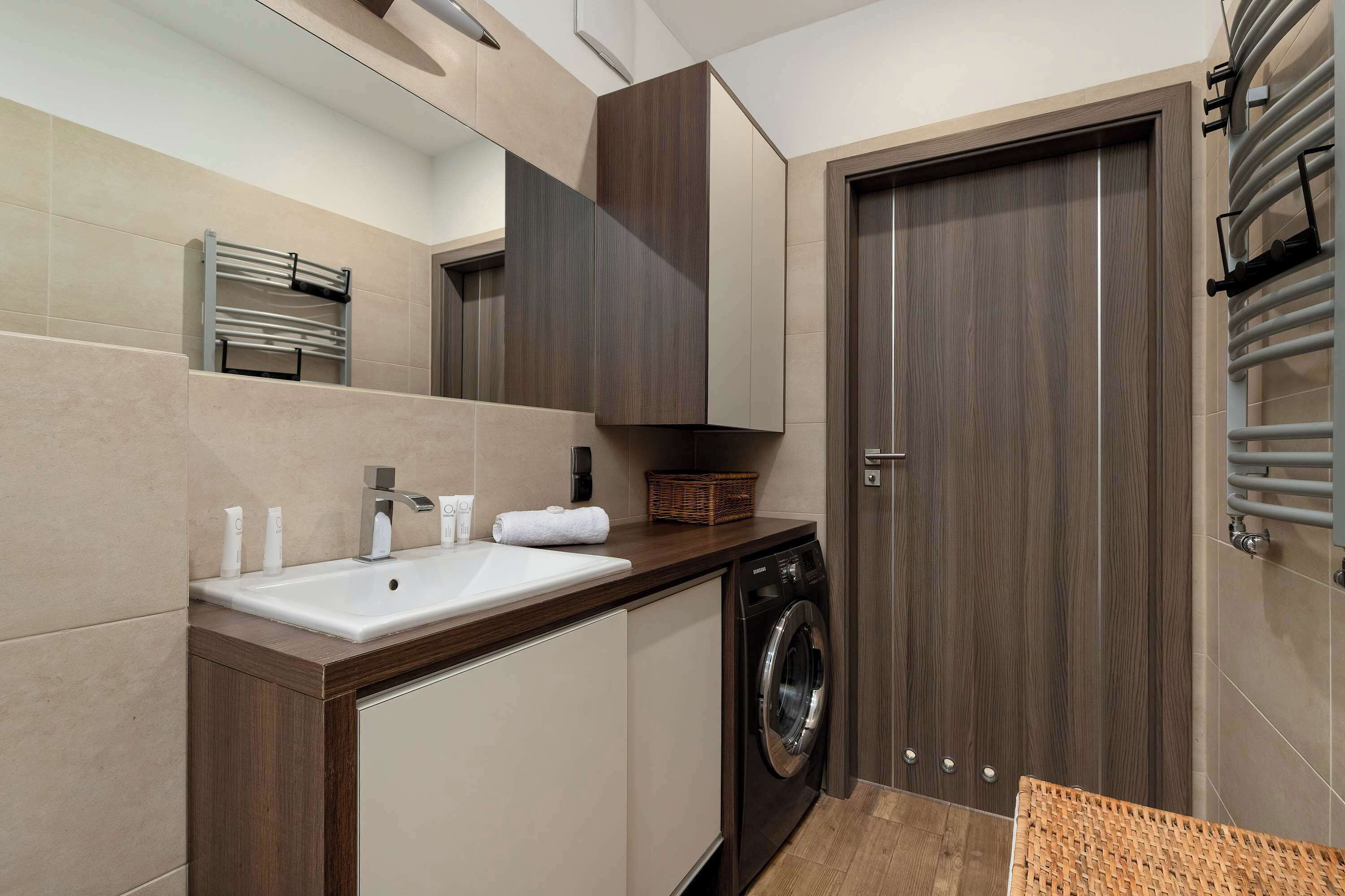 A modern bathroom with a sink, mirror, towel rack, and a wooden door.