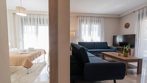 Moderni hotellihuone, jossa on sänky, sohva, televisio ja ruokapöytä.