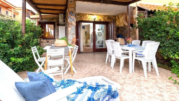 Un patio al aire libre con mobiliario blanco, una pared de piedra y techo de madera.