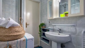 Un baño con un lavamanos blanco, un espejo, una toalla y una cesta.