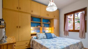 Un dormitorio con cama, armario, escritorio y ventana con cortinas.