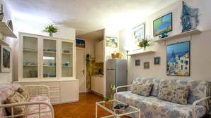 Una sala de estar con un sofá, una mesita, un armario y una zona de cocina al fondo.