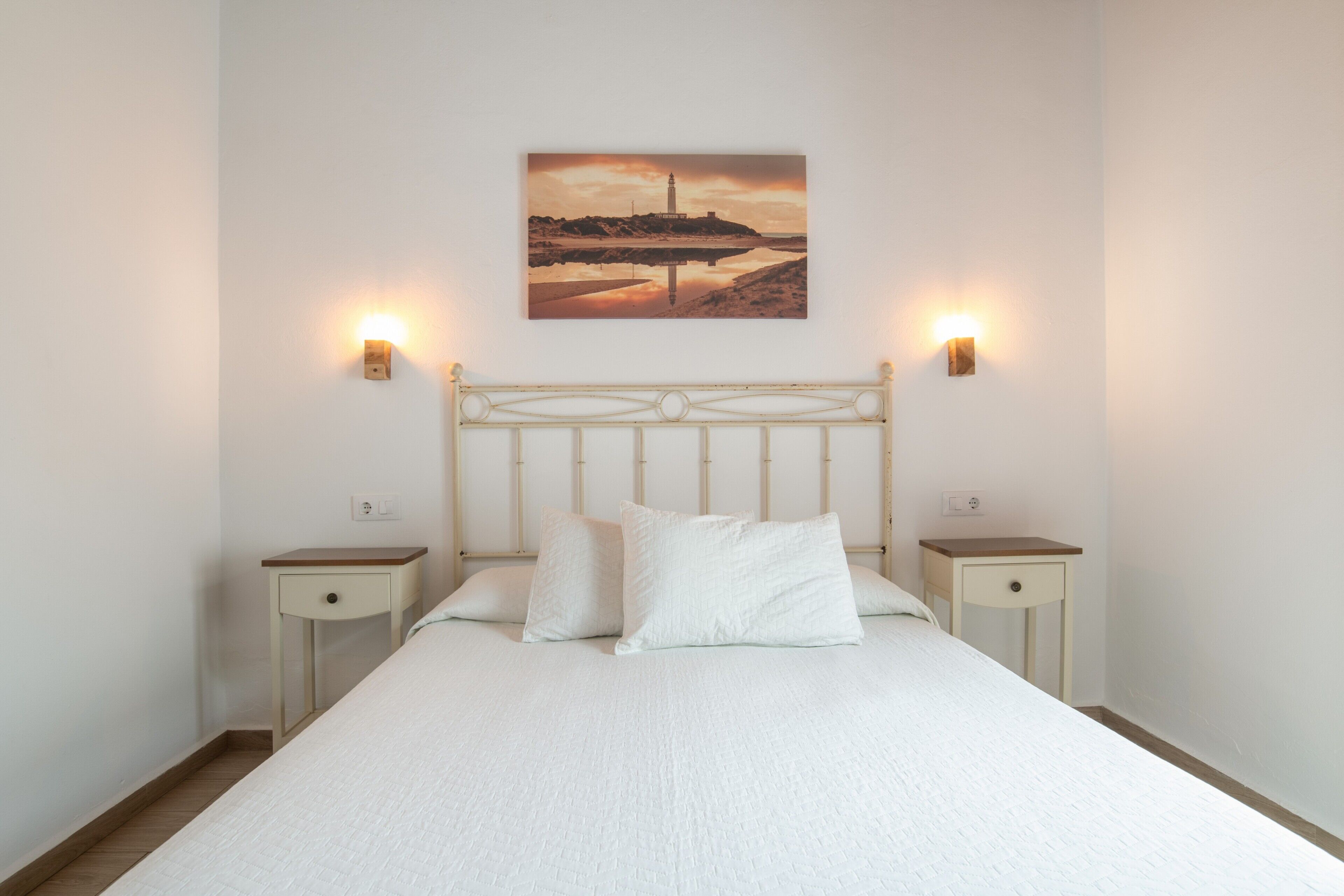 Un lit avec une tête de lit, deux tables de chevet et un tableau accroché au mur.