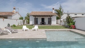 A swimming pool with lounge chairs, a small patio, and a white building with a tiled roof.