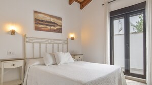 A bedroom with a bed, bedside tables, a painting, and a sliding glass door to the outside.