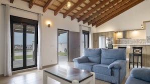 A modern living room with a sofa, a glass-top coffee table, and a kitchen area with appliances.