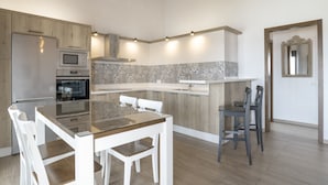 A modern kitchen with wooden cabinetry, a built-in oven, microwave, and a glass dining table with chairs.