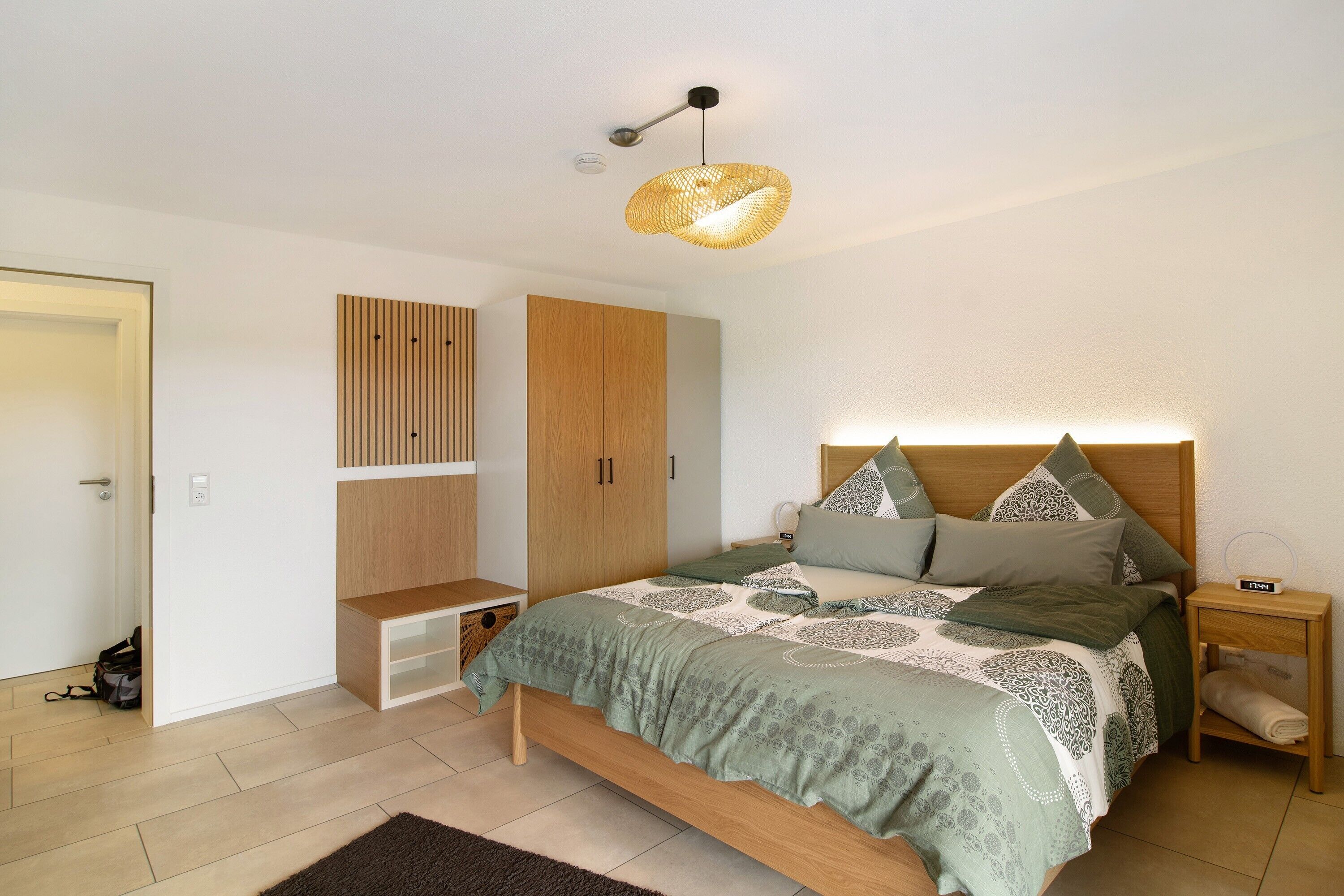 A bedroom with a bed, wooden wardrobe, bedside table, and a hanging light fixture.