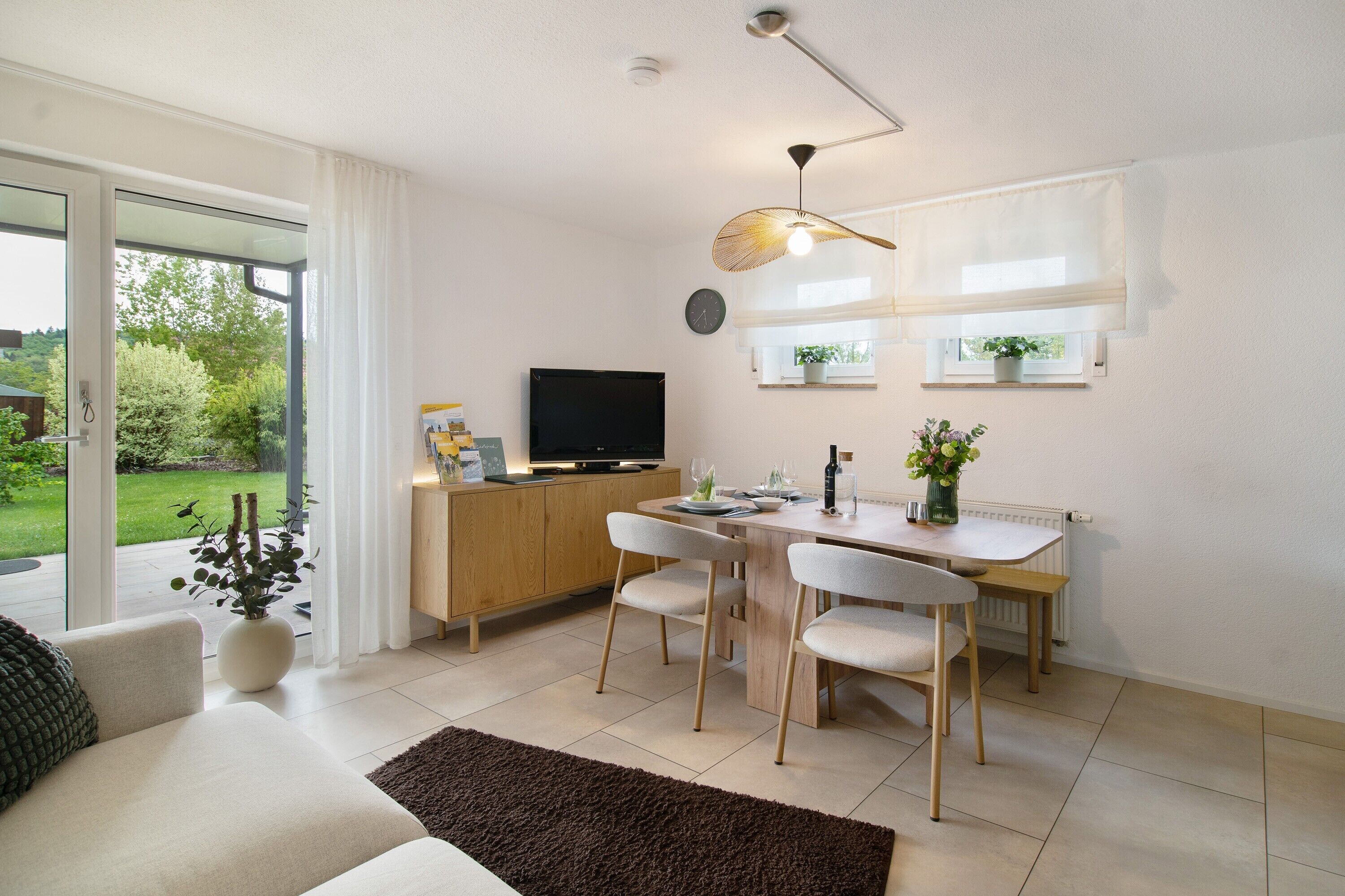 Ett modernt vardagsrum med en soffa, ett matbord, stolar, en tv och ett fönster med gardiner.