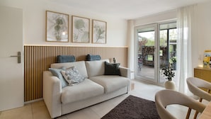 A modern living room with a sofa, a dining area with a chair, and a sliding glass door leading to an outdoor area.