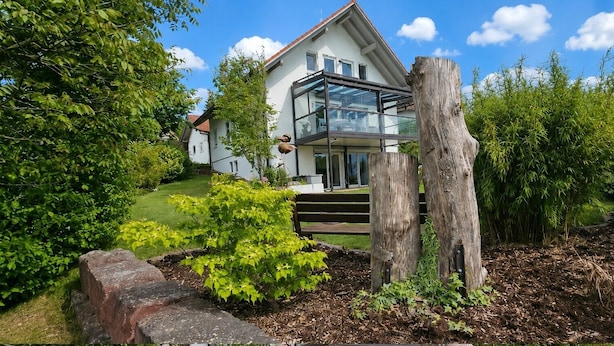 A modern house with a glass conservatory, surrounded by lush greenery and a well-maintained garden.