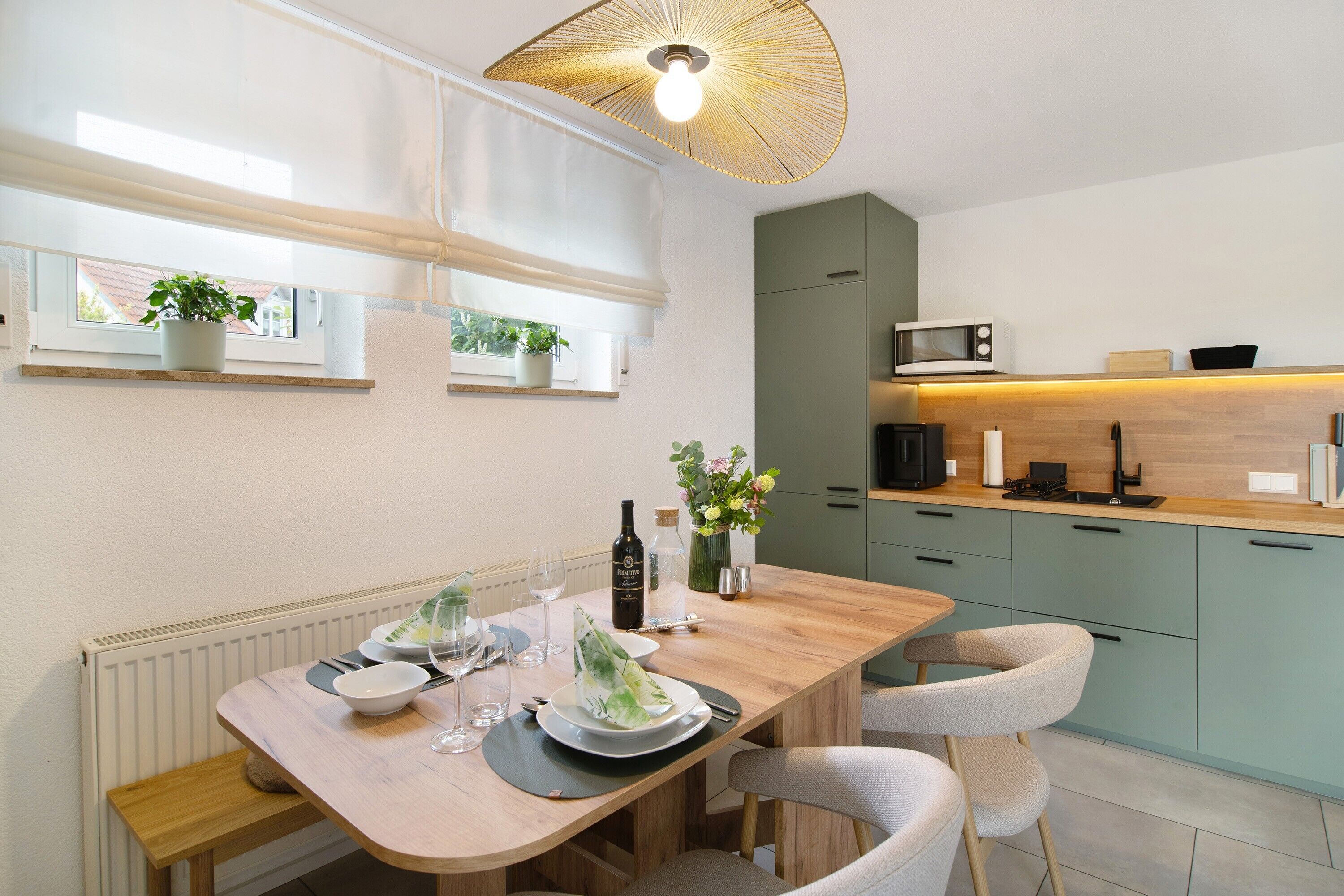 Een moderne keuken met een eettafel voor twee personen, een magnetron, en een potplant op het aanrecht.