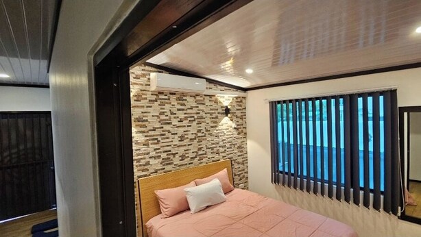 Quarto com cama, luminária na parede, janela com persianas e porta para outro cômodo.