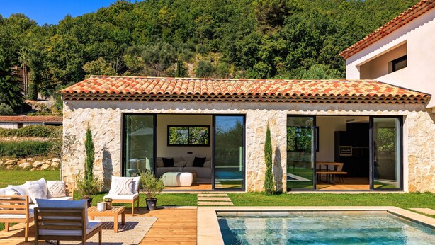 Ein modernes Haus mit Swimmingpool, Natursteinaußenwand und Terrasse mit Gartenmöbeln.