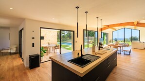 Eine moderne Küche mit Kochinsel, großen Fenstern und Blick auf Pool und Garten.