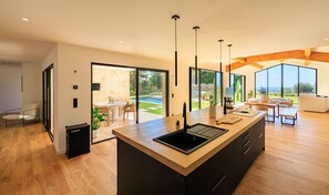 A modern kitchen with an island, large windows, and a view of a pool and garden. - Villa La Lumière – Évasion lumineuse & piscine (Tourretes sur Loup)