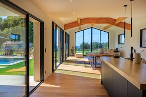 A modern kitchen with large windows, a wooden ceiling, and a view of a swimming pool. - Villa La Lumière – Évasion lumineuse & piscine (Tourretes sur Loup)