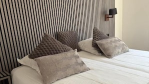 A bed with a striped headboard, a bedside lamp, and multiple pillows. - Giorgi Hôtel Restaurant (Bastogne)