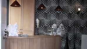A reception area with a wooden counter, zebra-patterned wallpaper, and pendant lighting. - Giorgi Hôtel Restaurant (Bastogne)
