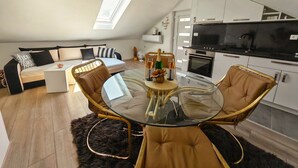 Ein modernes Loft-Apartment mit Schlafgalerie, einem Essbereich mit Glastisch und einer Küche mit schwarzer Arbeitsplatte.