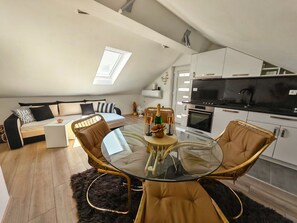 Ein modernes Loft-Apartment mit Schlafgalerie, einem Essbereich mit Glastisch und einer Küche mit schwarzer Arbeitsplatte.