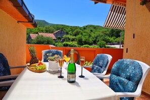A table set with fruits, a bottle of champagne, and glasses on a balcony with a view of green hills and buildings. - Holiday Home Rocca with pool (Vrgorac)