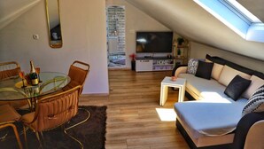Ein Dachgeschoss-Wohnraum mit Essbereich, einer Couch, einem Fernseher und einem Oberlicht.