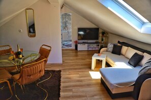Ein Dachgeschoss-Wohnraum mit Essbereich, einer Couch, einem Fernseher und einem Oberlicht.