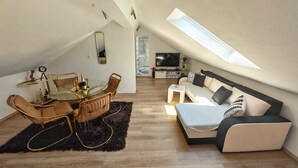 Ein modernes Loft mit Essbereich, einer Sofagarnitur, einem Fernseher und einem großen Fenster.