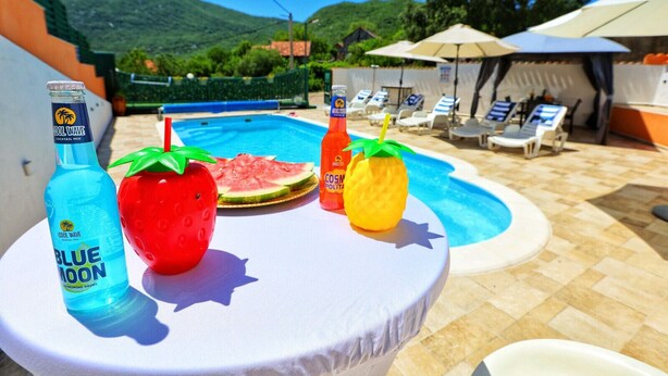 Ein Tisch am Pool mit einer Flasche Cool Wave Blue Moon, einem Wassermelonenscheibchen und einem Ananasausschank.