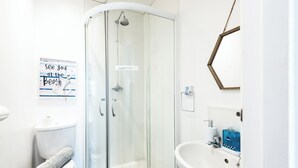 Une salle de bain avec une douche en verre, des toilettes avec une serviette à disposition, un lavabo avec un miroir et un panneau affiché sur le mur.