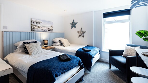 Une chambre avec deux lits, un bureau, une chaise et une grande fenêtre.