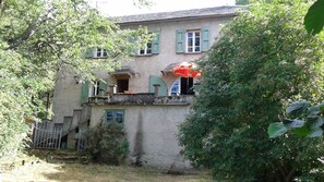 A two-story house with a balcony, a small garden, and a red umbrella. - House in the green (Vézins-de-Lévézou)
