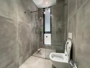 A modern bathroom with a glass shower enclosure, a toilet, and a small window. - Comfort Center Studio Apartments (Tirana)