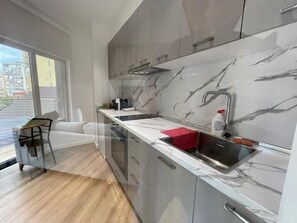 A modern kitchen with marble countertops, stainless steel appliances, and a view through a large window. - Comfort Center Studio Apartments (Tirana)