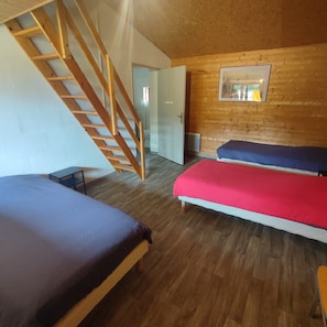 Una habitación con dos camas, una escalera de madera y una puerta que da a otra estancia.