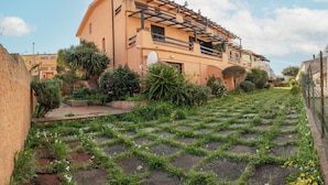 A residential building with a sloped roof, a balcony, and a garden with grass and small plants. - Casa Mara - 10 minutes from the beach (Porto Pozzo)