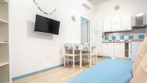 A room with a bed, a TV mounted on the wall, a small table with chairs, a kitchen area with cabinets, and a mirror. - Casa Mara - 10 minutes from the beach (Porto Pozzo)