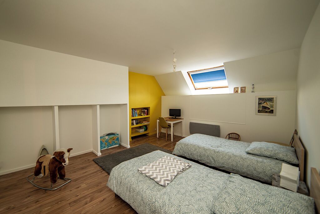 A bedroom with two beds, a desk, a rocking horse, and a bookshelf.