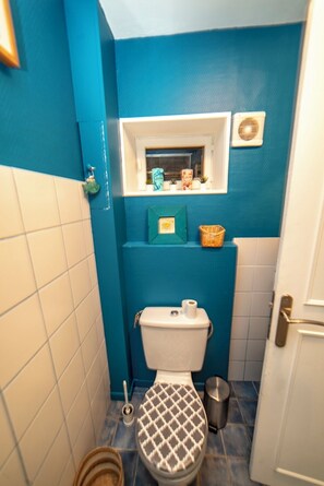 A bathroom with a toilet, a bidet, a small shelf with toiletries, and a window above the toilet. - Large 8-person vacation home, 5 minutes' walk from the sea. (Langrune-sur-Mer)
