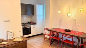 A modern kitchen with white cabinets, a stove, and a dining area with a red table and chairs. - Villa Elisa - Ottavia Apartment near Venice with garden and parking (Spinea)