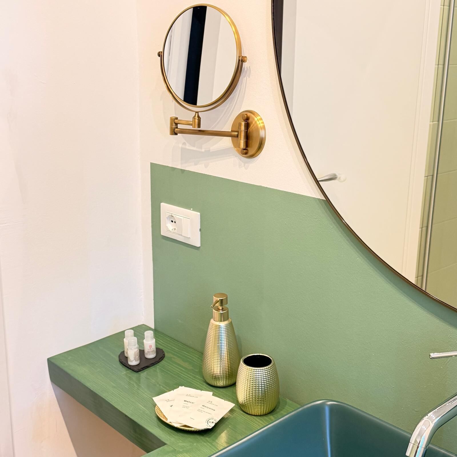 A bathroom with a green vanity, a gold-framed mirror, a sink, and toiletries.