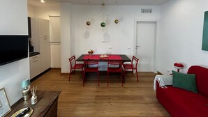 A modern kitchen with white cabinets, a dining table with red chairs, and a red sofa in the living area. - Villa Elisa - Ottavia Apartment near Venice with garden and parking (Spinea)