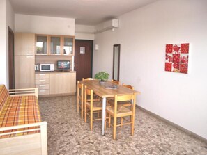A compact living space with a kitchenette, a dining table with chairs, a sofa, and a potted plant. - Ideal Getaway Flat in Lignano (Lignano Sabbiadoro)