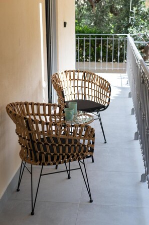 A balcony with wicker chairs and a glass table, a metal railing, and a view of greenery. - Ruby’s House Apartment with Balcony, Wi-Fi and Air Conditioning (Glifada)