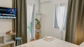 Quarto de hotel com cama, televisão, planta e janela com cortinas.