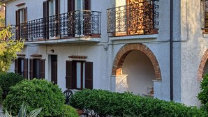 Un edificio de dos plantas con ventanas arqueadas y balcones, rodeado de vegetación cuidada.