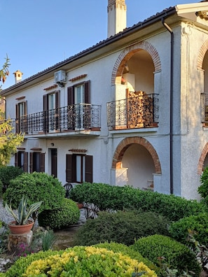 A two-story building with arched windows and balconies, surrounded by well-maintained greenery.