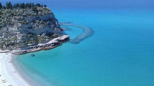 Un paisaje costero con una playa, acantilados rocosos y aguas azules cristalinas.