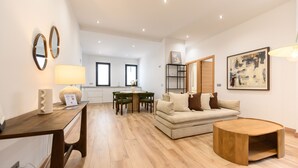 A modern living room with a wooden coffee table, a sofa, a dining table with chairs, and a kitchen area in the background. - (DDS1014) 2 bedroom apartment in Goya, Salamanca District (Madrid)